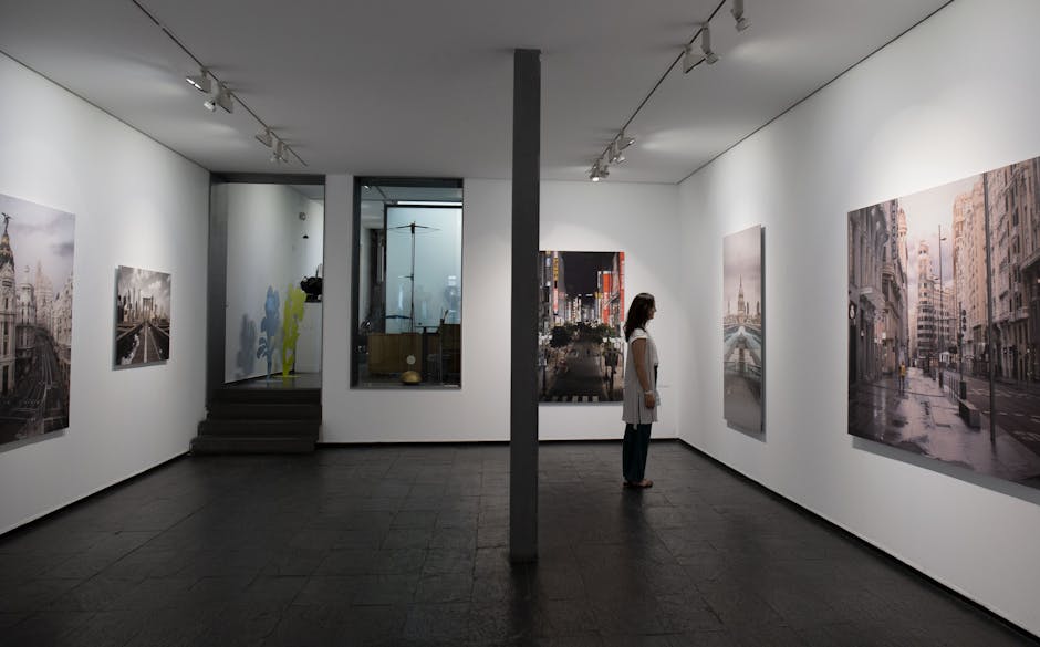A woman observes urban landscape paintings in a Madrid art gallery, showcasing contemporary urban art.